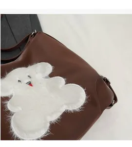 Detail of a brown PU tote with a cute white plush animal patch and silver hardware