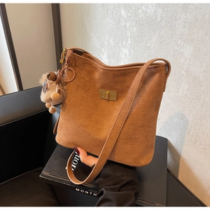 Detail of brown faux suede bucket bag featuring a gold clasp and soft fur pompom charm