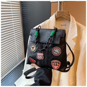 Macro detail of black leather backpack with vintage embroidery patches and green rope handle