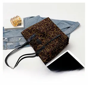 Detail view of leopard print tote bag with black handles next to a laptop and books