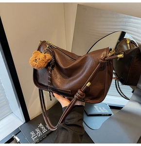Λεπτομέρεια vintage καφέ δερμάτινης τσάντας ώμου με κρεμαστό αρκουδάκι και χρυσά στοιχεία