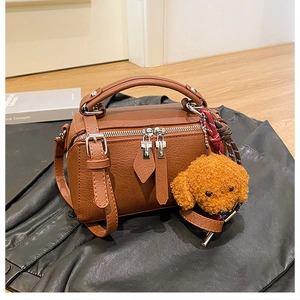 Détail du sac polochon marron texture grainée avec une breloque caniche en peluche