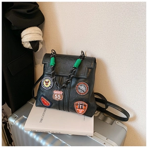 Detail of vintage black leather backpack featuring colorful embroidered patches and woven handle