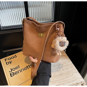Detailed view of brown suede bucket bag with gold lock and plush bear charm accessory