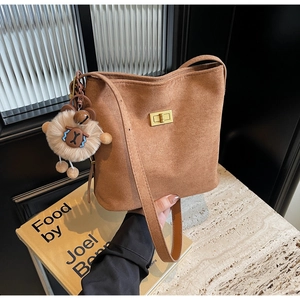 Detail of brown faux suede bucket bag featuring a gold clasp and a plush lion charm