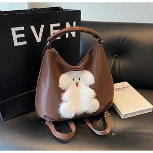 Detail of glossy brown faux leather tote with white plush puppy patch and straps