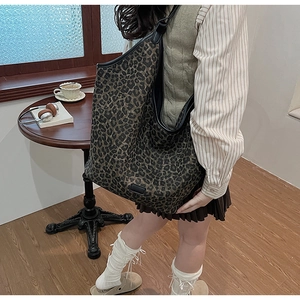 Large leopard print tote bag with black leather straps shown in a cozy coffee shop setting