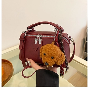 Détail du sac polochon bordeaux avec un charm de chien en peluche et fermeture éclair