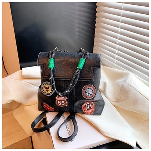 Detail of vintage black leather backpack showing colorful patches and woven handle
