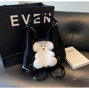 Detail of glossy black tote bag featuring a white plush cartoon bear charm on soft leather