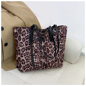 Macro detail of large leopard print tote bag on sofa with black leather strap accents