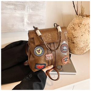 Detail of vintage brown leather backpack with collegiate patches and woven rope handle