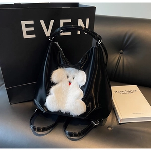 Detail of glossy black patent leather bag with white plush bear and silver hardware