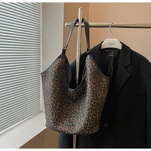Detailed view of leopard print tote bag with black leather trim hanging on a hanger