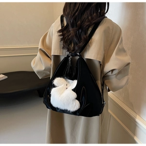 Detail of black glossy tote bag worn as a backpack with a plush white animal charm