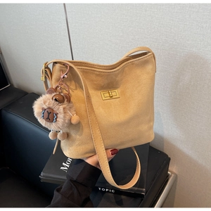 Macro shot of khaki suede bucket bag featuring a gold twist lock and plush bear charm