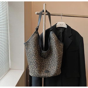 Detail of leopard print tote bag with black leather straps hanging in a minimalist setting