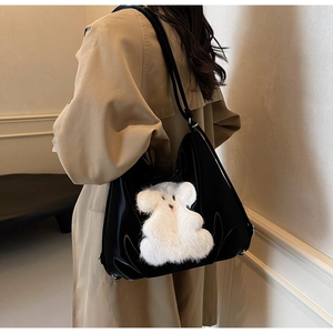 Detail showing the glossy black material and white faux fur bear on the tote bag