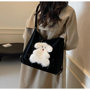 Close-up of the plush white dog patch on the black glossy leather tote bag surface