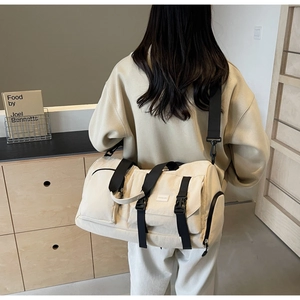 Vue arrière d'un mannequin portant un grand sac de voyage crème avec des sangles noires robustes
