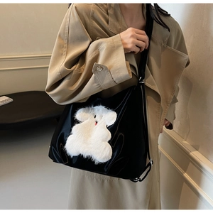 Detail of black glossy tote bag with a white plush teddy bear applique on shoulder strap