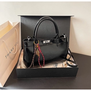 Détail d'un sac à main vintage noir avec fermoir rotatif argenté et pendentif tressé
