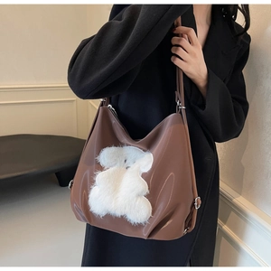 Close-up of brown glossy leather tote bag featuring a cute white plush bear decoration