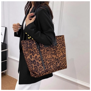 Close-up of leopard print tote bag with black straps worn over a black blazer
