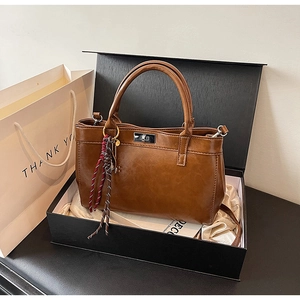 Sac à main marron avec fermoir rotatif argenté et pompon dans une boîte cadeau