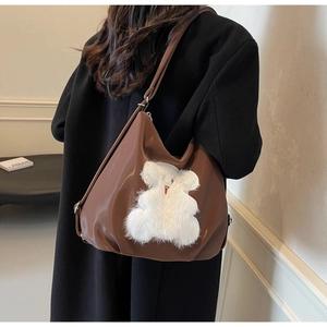Detail of glossy brown tote bag with white plush bear and slim shoulder strap