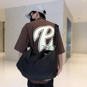 Rear view of a large black nylon crossbody fitness bag worn by a street style model