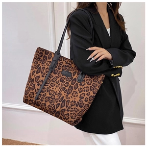Side view of a large leopard print tote bag with black leather straps on a model