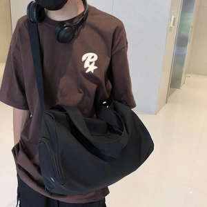 Close-up of black cylinder sports duffel bag with wide adjustable shoulder strap on model