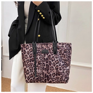Detailed view of leopard print tote bag with black leather straps and brand plate