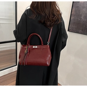 Détail du sac à main bordeaux avec fermoir métallique et pendentif tressé élégant