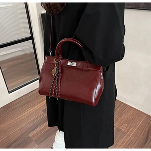 Détail d'un sac à main bordeaux avec fermoir argenté et breloque tressée décorative