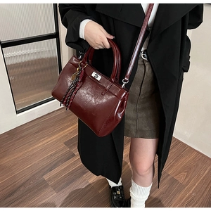Détail du sac à main en cuir bordeaux avec fermoir rotatif et pompon décoratif