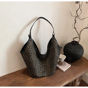 Detail of leopard print tote bag featuring wide black leather straps on a wooden table