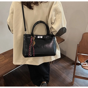 Détail d'un sac à main noir en cuir avec fermoir rotatif argenté et pompon tissé