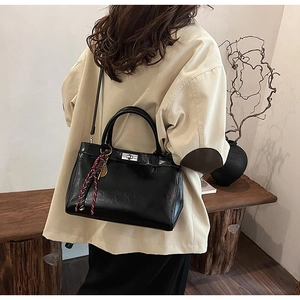 Sac à main noir brillant avec fermoir rotatif argenté et cordon tressé porté par un mannequin
