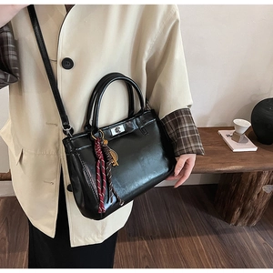 Détail du sac en cuir noir brillant avec fermoir rotatif argenté et pompon tissé élégant