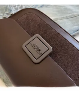 Close-up of square metal buckle on dark brown leather crossbody bag with stitching