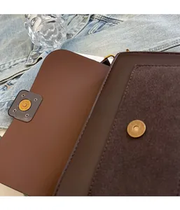 Close-up of magnetic buckle and dark brown leather textures on minimalist square bag