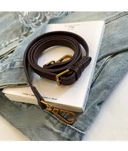 Detail of adjustable dark brown leather strap with matte gold buckle on a book