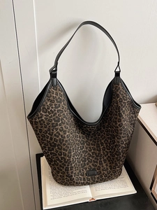 Large leopard print tote bag with black leather trim shown on an open book background