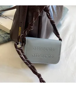 Detailed macro of dark brown leather bag with MUCOOU embossed mini pouch and woven strap