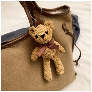 Detailed view of hand-crocheted bear pendant with silk bow on a brown canvas tote bag
