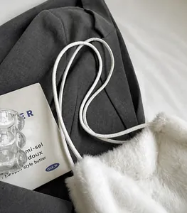 Close-up of white faux fur shoulder bag with leather strap on grey blazer