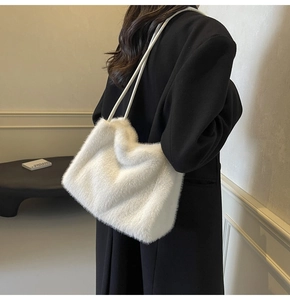 Close-up of white plush faux fur shoulder bag with minimalist straps on dark coat