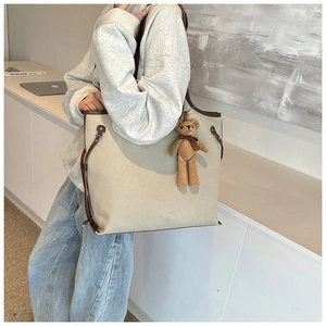 Detail of beige canvas tote bag with brown leather trim and cute plush bear charm